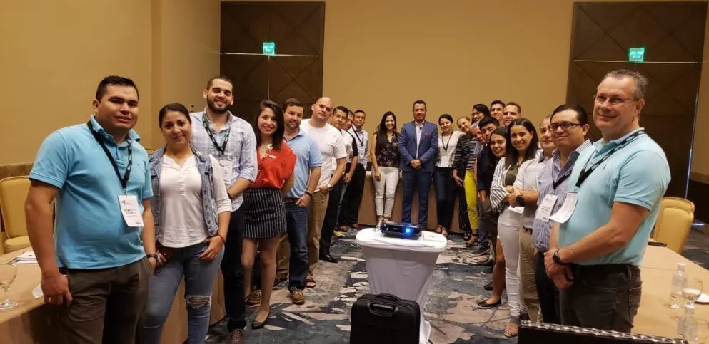 Grupo de profesionales en un salón de eventos escuchando atentamente al capacitador que explica un diagrama en la pantalla