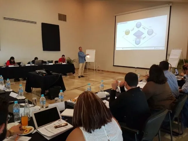 Conferencia de profesionales participando activamente en un curso de liderazgo, donde el instructor presenta conceptos